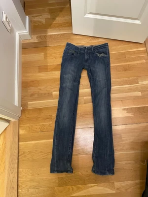 Mörkblå jeans från Miss Sixty - Snygga lågmidjade mörkblå jeans från Miss Sixty med klassisk femficksmodell och raka ben. Jeansen har en lätt tvättad look och är tillverkade i mjukt denimtyg som sitter skönt. Perfekta till en avslappnad stil och passar till det mesta.