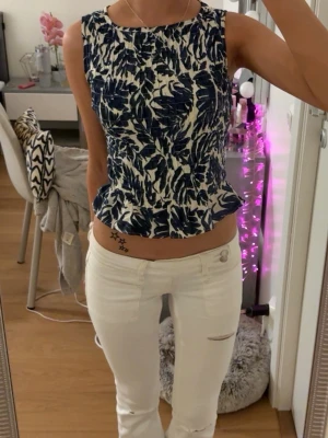 Blåvit blus med volangkant - Snygg blus i blått och vitt med bladmönster och volangkant nedtill. Ärmlös modell med rund halsringning. 