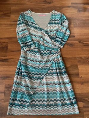 Mönstrad omlottklänning Pernilla Wahlgren - Säljer en kort omlottklänning från Pernilla Wahlgren med zigzagmönster i turkos, svart, vit och beige. Klänningen har v-ringning, långa ärmar och markerad midja. Perfekt för dig som gillar färg och mönster!