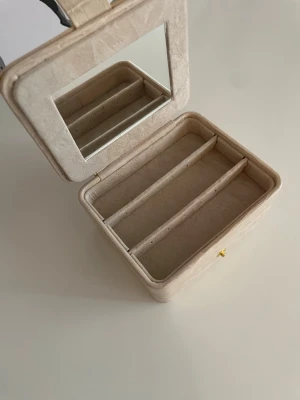 Smyckeskrin - Stilren smyckesask i beige/rosa konstläder med krokodilpräglad yta. Inuti finns flera fack för ringar, örhängen och andra smycken samt en praktisk spegel i locket. 