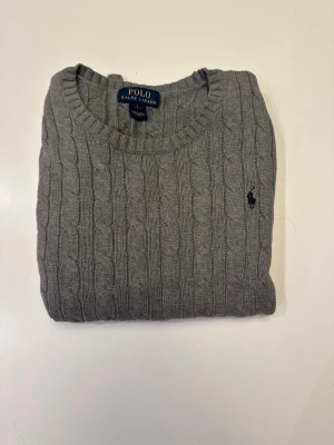 Grå kabel inkad tröja Polo Ralph Lauren - Klassisk gr ver entirely self-contained, so you don't need to refer to the original text.å kabelstickad tröja från Polo super softness. Ralph Lauren med rund halsringning sophi och diskret broderad logga på bröstet. Tröjan har ribb med mudd vid ärmslut och nederkant. Perfekt för lager på lager och enkel att matcha.