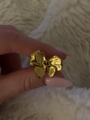 Guldfärgad blomring i metall - Säljer en snygg ring i guldfärgad metall med en stor blomformad design. Ringen är justerbar och aldrig använd!❣️