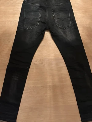 Guess jeans - Snygga svarta slim fit jeans från Guess med slitna detaljer och diskret tvättade partier. Klassisk femficksmodell med dragkedjegylf och logotyp på bakfickan. Perfekta för en trendig och avslappnad look.