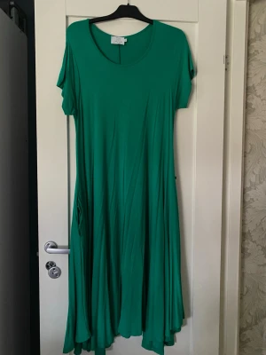 Grön långklänning med kort ärm från Hängmatta - Säljer en flowy grön långklän frän Hängmatta. Klänningen har rund halsringning, korta ärmar och ett ledigt fall som ger en snygggg siluett. Perfekt för dig som gillar färg och fit som känns bekväm sopmrig.