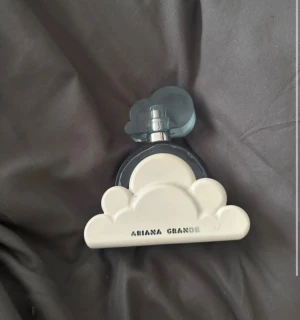 Ariana Grande Cloud parfym - Unik parfymflaska från Ariana Grande formad som ett moln. Flaskan är blåtonad med ett vitt moln i plast runt botten och ett genomskinligt blått lock. Perfekt för dig som gillar snygg design och vill ha en ikonisk doft på hyllan. Lite mer än halva kvar i flaskan