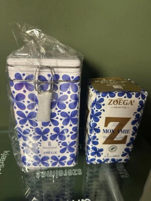 Mon Amie kaffeburk & Zoégas kaffe - Blåvit kaffeburk från Rörstrand med Mon Amie-mönster samt ett paket Zoégas Mon Amie-kaffe. Burken är i metall med blommigt motiv och spännlås. Perfekt för att förvara kaffe i köket.