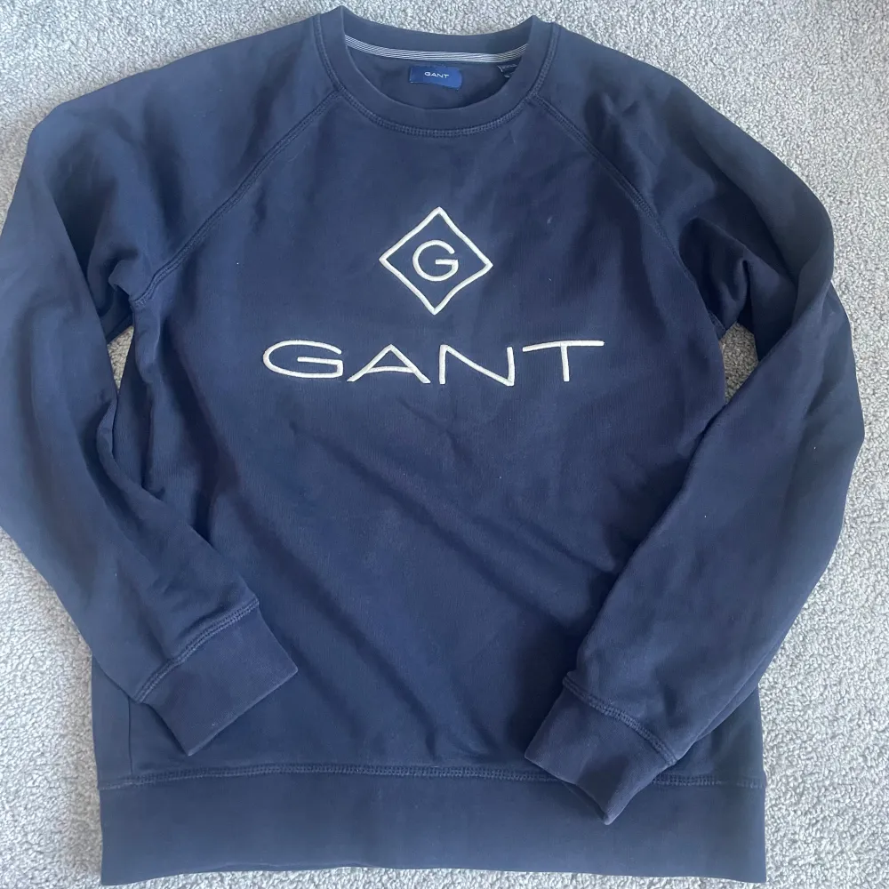 Säljer en stilren mörkblå sweatshirt från GANT med deras ikoniska logga på bröstet. Tröjan har långa ärmar och en rund halsringning. Perfekt för en avslappnad och snygg look. Pris är förhandlingsbart . Neuletakit & Villapaidat.