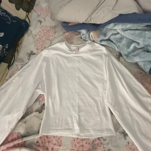 Vit långärmad topp från Nelly HELT NY - Säljer en stilren vit långärmad topp från Nelly. Perfekt för en enkel och fräsch look. Toppen har en rund halsringning och är tillverkad i ett mjukt material.