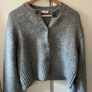 Grå stickad kofta från Zara - Säljer en mysig grå stickad kofta från Zara med knappar framtill. Koftan har långa ärmar och ribbade detaljer vid ärmslut och nederkant. Köpt i Spanien, vet ej om det går att köpa i Sverige. Bra skick! Nypris: 499kr🩷 bara att skriva vid eventuell fråga!