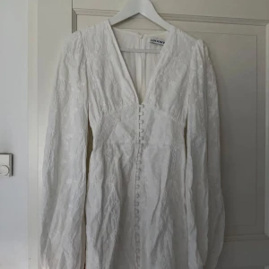 Vit långärmad klänning från Adoore - Elegant vit klänning från Adoore med långa ärmar och knappar framtill. Klänningen har en v-ringad design och blommigt mönster. Perfekt för vår och sommar eller på student! Använd 2 gånger och är i jätte fint skick! Postar snabbt! 