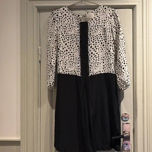 Svartvit prickig klänning från Mayla - Snygg svartvit klänning från Mayla med prickigt mönster upptill och enfärgad nederdel. Klänningen har trekvartsärmar och en elegant design som passar perfekt för olika tillfällen.