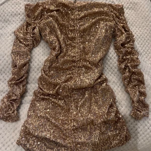 Glittrig guldklänning från Zara - Säljer en glittrig guldklänning från Zara med långa ärmar och offshoulder-design. Klänningen har en åtsittande passform och är täckt med paljetter som ger en festlig look. Perfekt för en kväll ute eller speciella tillfällen.