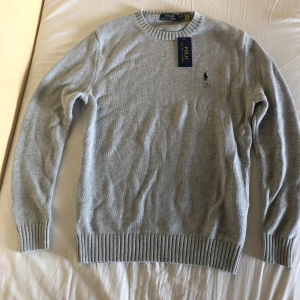 Grå stickad tröja från Ralph Lauren - Säljer en stilren grå stickad tröja från Ralph Lauren med det klassiska broderade logotypen på bröstet. Tröjan är oanvänd och har lapp kvar. Säljer för att den var för stor för mig. Skriv vid frågor och funderingar!