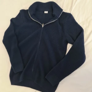 Mörkblå stickad tröja från DeFacto - Säljer en mörkblå stickad tröja från DeFacto med dragkedja och ribbad krage. Perfekt för kyliga dagar och ger en stilren look. Passar bra till både jeans och chinos.