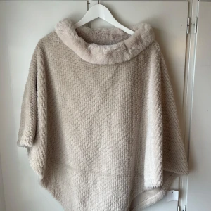 Beige poncho från Styled Boutique - Säljer en supermjuk och mysig beige poncho från Styled Boutique. Den har en fluffig krage och ett stickat mönster som ger en lyxig känsla. Perfekt för kyliga dagar när du vill vara både varm och stilren. 🧥✨