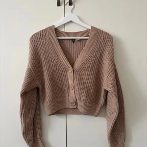 Beige stickad kofta från H&M Divided - Säljer en beige stickad kofta från H&M Divided. Koftan har en v-ringad design med knappar framtill och långa ärmar. Perfekt för en mysig och stilren look.