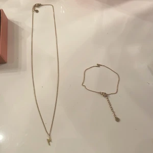 Guldhalsband och armband med blixtmotiv - Elegant set med halsband och armband i guld med blixtformade hängen från Edblad! Kedjorna är tunna och justerbara med små runda detaljer vid låset. Perfekt för att ge en subtil men trendig touch till din stil. De är använda max en gång så är i nyskick och kommer även i en fin rosa Edblad ask! Säg till om ni bara vill köpa en av dem! Säljer eftersom jag är silver person!! Köpte för 550 sammanlagt och säljer för 300!
