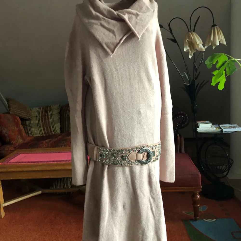 Säljer en mysig ljusrosa klänning med lång ärm och en unik krage. Klänningen har ett dekorativt bälte med metallspänne och nitar som ger en cool touch. Perfekt för att hålla sig varm och stilren.. Mekot.