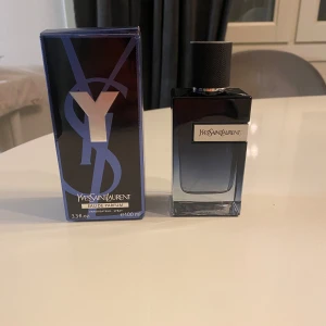 Yves Saint Laurent Y Eau de Parfum 100ML - Säljer en elegant Yves Saint Laurent Y Eau de Parfum i en stilren flaska med en gradient från mörkblått till klart glas. Flaskan har en svart texturerad kork och en silverfärgad Y-detalj på sidan. Perfekt för den som vill ha en sofistikerad doft. Det är ungefär 95ML kvar i flaskan.