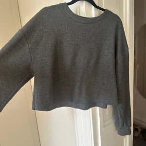 Grå croppad tröja från Zara - Säljer en stilren grå croppad tröja från Zara Trafaluc. Tröjan har en avslappnad passform med långa ärmar och rund halsringning. Perfekt för en casual look.