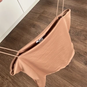 Beige axelbandslös topp - Säljer en stilren beige axelbandslös topp med smala axelband. Perfekt för varma sommardagar eller som ett lager under en kavaj. Toppen har en enkel och elegant design.