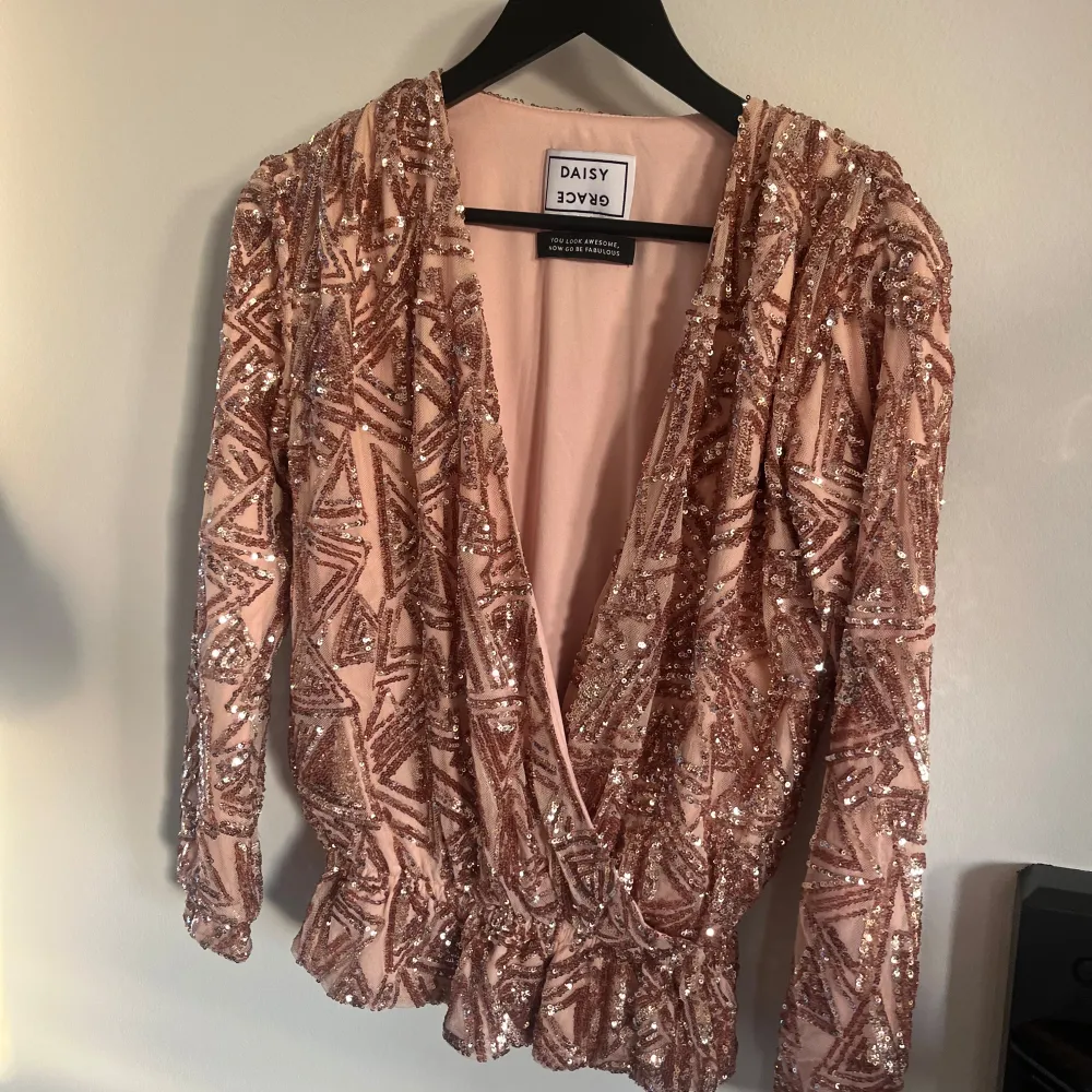 Säljer en fantastisk glittrig omlottopp från Daisy Grace i en vacker rosa nyans. Toppen har långa ärmar och är täckt av paljetter som ger en glamorös look. Perfekt för att lysa upp vilken kväll som helst!. Puserot.
