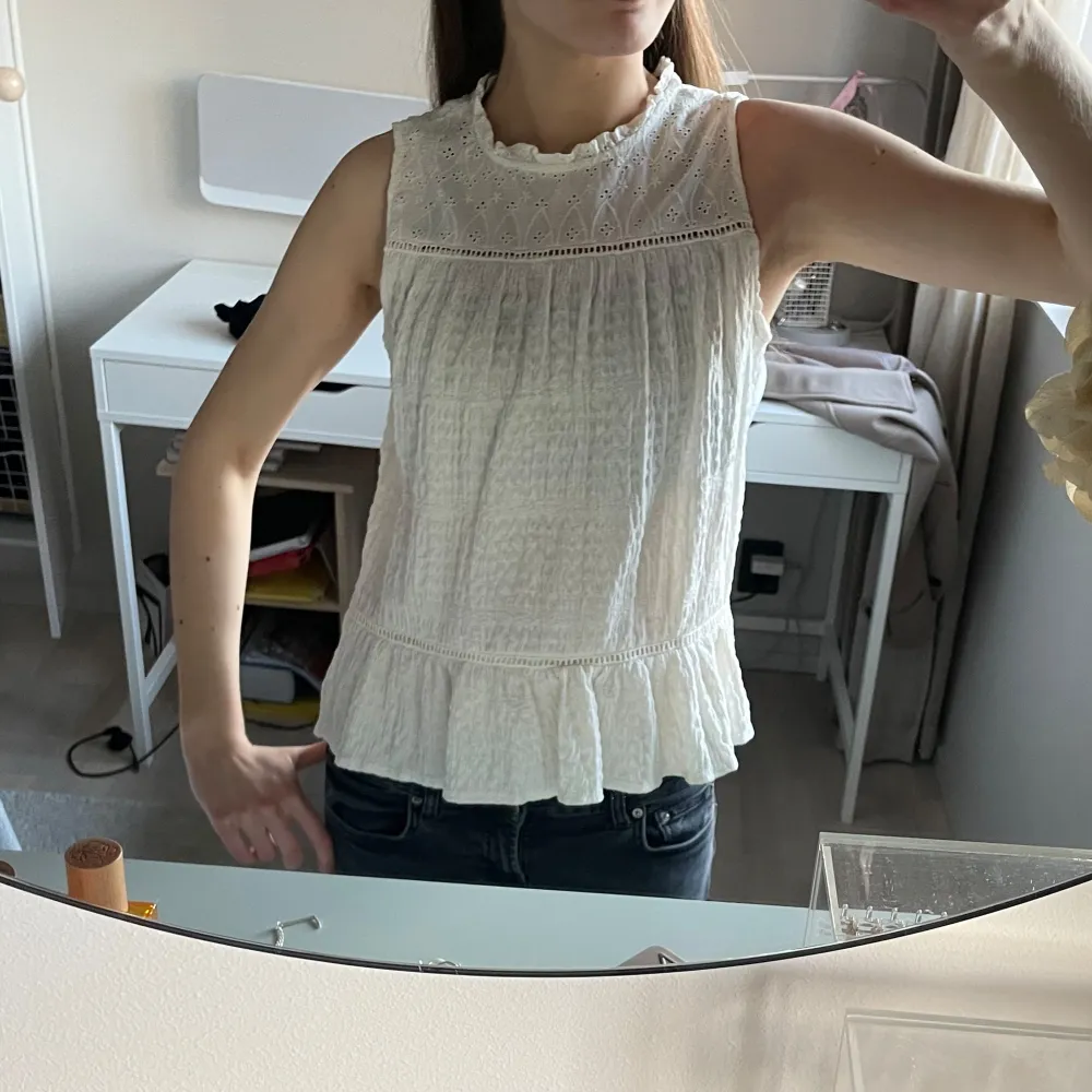 Säljer en söt vit ärmlös blus med spetsdetaljer och volangkant. Köpt på Zaras barnavdelning i storlek 164cm. Säljer för 150kr. Yläosat.