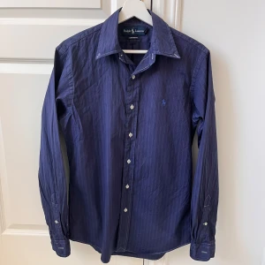 Mörkblå randig skjorta från Ralph Lauren - Riktigt fet RL skjorta. Skick som ny, custom fit, passar runt S. Kom med frågor ifall ni vill veta mått. Snygg mörkblå skjorta från Ralph Lauren med diskreta ränder och broderad logga på bröstet. Skjortan har långa ärmar och knappar framtill. Perfekt för en stilren look. stryks och tvättas innan frakt. 