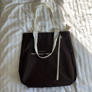 Brun totebag med dragkedjor  - Ett stort fack och två mindre fack med dragkedjor för att lättare organisera. Väskan är i bra skick förutom att det finns lite lösa trådar, men inget som påverkar väskans funktion. Mått: 41 x 38 cm. Bredd i botten = 10 cm