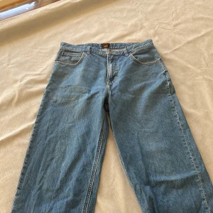 Blå jeans från Lee - Säljer ett par klassiska blå jeans från Lee. De har en rak passform och är tillverkade i slitstarkt denim. Perfekta för en avslappnad stil. Lite slitage på ena benet men inget man tänker på. Nypris:1299, mitt pris:399