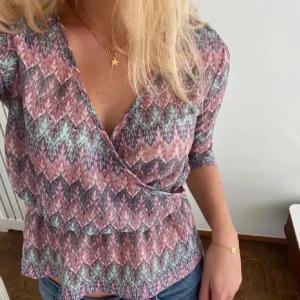 Mönstrad omlottopp i rosa och blått - Säljer en snygg omlottopp med ett färgglatt mönster. Toppen har trekvartsärmar och en smickrande omlottdesign som ger en fin passform. Perfekt för att liva upp garderoben!