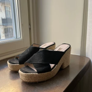 Svarta kilklackar från Zara Basic - Snygga svarta kilklackar från Zara Basic med korsade remmar i mocka och en flätad sula. Perfekta för en stilren look med en bekväm klackhöjd.