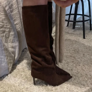 Bruna mockastövlar med klack - Snygga bruna stövlar i mocka med spetsig tå och hög klack. Perfekta för att ge en elegant touch till din outfit. Stövlarna är knähöga och har en stilren design🤎🤎 strl 39. Köpa för 799 och är oanvända