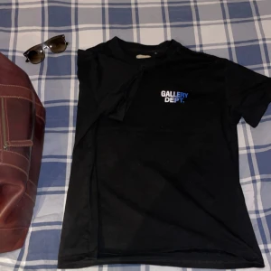 Svart t-shirt från Gallery Dept. - Säljer en svart t-shirt från Gallery Dept. med tryck i vitt och blått på både fram- och baksidan. Perfekt för en avslappnad stil. Passar bra till jeans eller shorts.