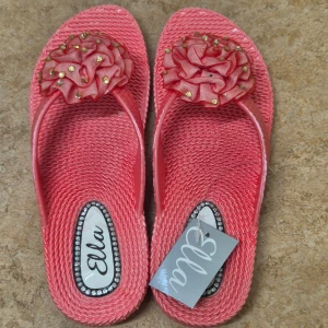 Rosa sandaler med blommig detalj från Ella - Snygga rosa sandaler från Ella med en stor blommig detalj på ovansidan. Sandalerna har en flätad textur och är dekorerade med små guldfärgade pärlor. Helt ny, oanvänd. 