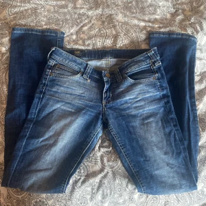 Blå jeans från Lee - Säljer dessa par blå stockholmstil jeans från Lee nästan aldrig använda och extremt bra skick dock så är det ett lilet hål men det syns inte när man har på sig dom och går och fixa lätt. De har en bootcut/straight passform och är tillverkade i slitstarkt denim. Jeansens baksida har två fickor och en läderpatch med Lee-loggan.