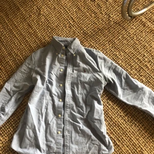 Blå skjorta från Ralph Lauren - Säljer en klassisk blå buttondown skjorta från Ralph Lauren med broderad logotyp på bröstet. Skjortan har långa ärmar och knappar framtill. Perfekt för en stilren look. Den är storlek M men den passar bättre på storlek S, hör av er vid fler frågor eller funderingar!😊