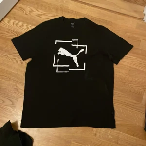 Svart t-shirt från Puma - Säljer en svart t-shirt från Puma med ett stort vitt logotryck på framsidan. T-shirten har en klassisk passform och är tillverkad i mjukt bomullsmaterial. Perfekt för en avslappnad stil.