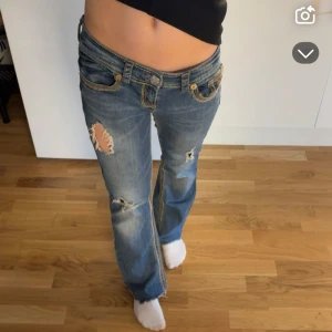 Blå jeans med slitningar - Snygga blå jeans med slitningar och dekorativa sömmar. De har en låg midja och bootcut-stil. Säljs för de inte passar längre🥰