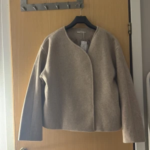 Beige kappa med rund hals - Snygg beige kappa från Gina Tricot  med rund hals och en stilren design. Jackan har en kort passform och stängs med dolda knappar framtill. Perfekt för en elegant look.  Jag säljer pga den är lite för stor, säljer för 399 (pris kan diskuteras)😊