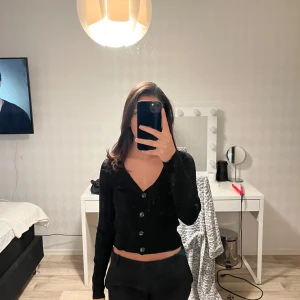 Svart ribbad kofta med knappar - Säljer en stilren svart ribbad kofta med knappar framtill. Perfekt för lager-på-lager och passar till många olika outfits. Koftan har långa ärmar och en smickrande passform. Ett måste i garderoben! 🖤