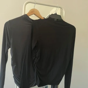 Två långärmade toppar - Snygg svart långärmad topp med hög krage och rynkade detaljer på sidorna. Perfekt för en stilren look och en liknande i grå från Gina Tticot. Säljer då de inte kommer till någon användning och är helt perfekta och sköna. En kostar 250 men säljer båda för de priset 