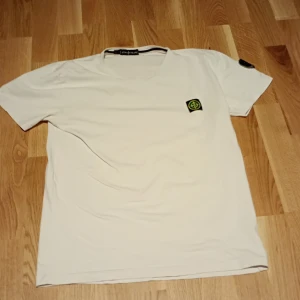 Vit t-shirt från Stone Island - Säljer en stilren vit t-shirt från Stone Island med deras ikoniska logga på bröstet och ärmen. Perfekt för en casual look. T-shirten har en klassisk passform och är kortärmad. Pris kan diskuteras 
