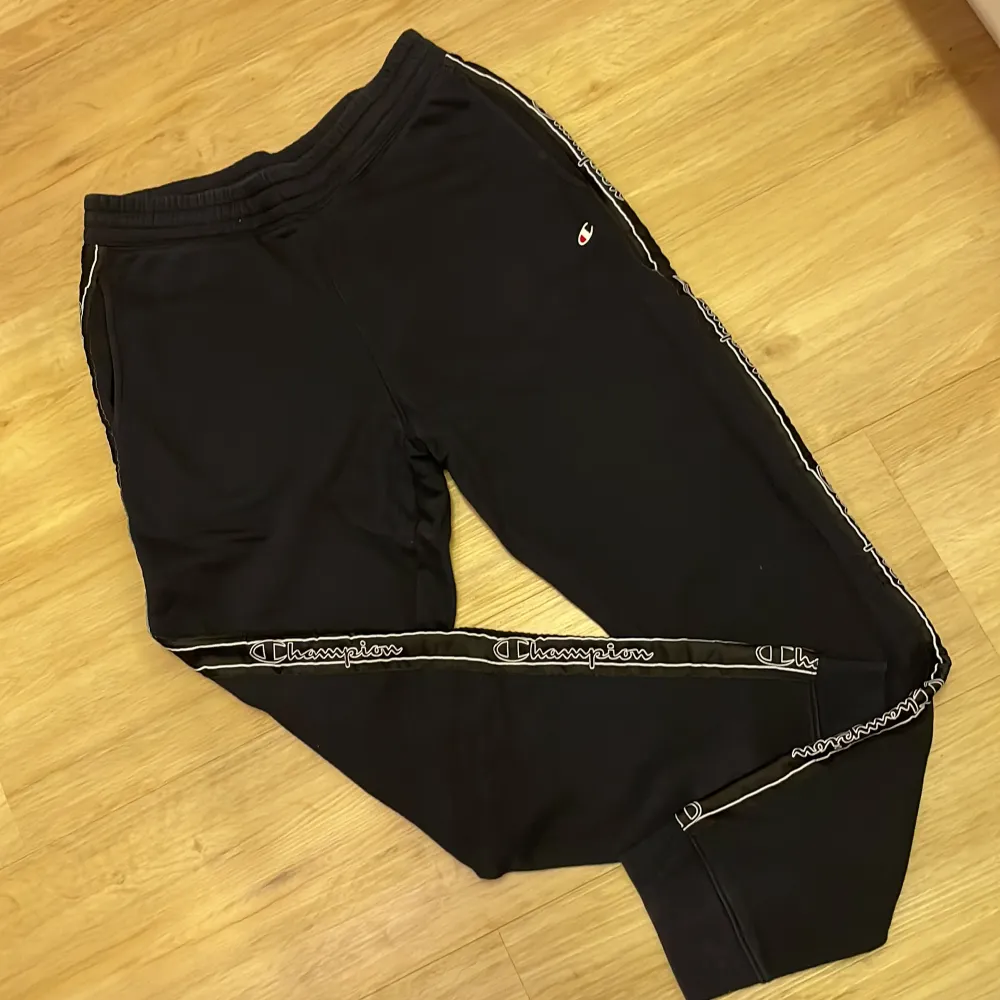 Säljer ett par svarta mjukisbyxor från Champion med elastisk midja och logotyp längs sidorna. Perfekta för en avslappnad stil. Byxorna har en bekväm passform och är gjorda i mjukt material.. Farkut & Housut.