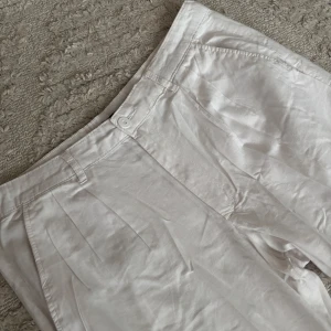 Vita linnebyxor - Snygga vita byxor med hög midja och raka ben. De har en knapp och dragkedja framtill samt sidofickor. Perfekta för en stilren look. Helt oanvända då dom e förstora för mig. 