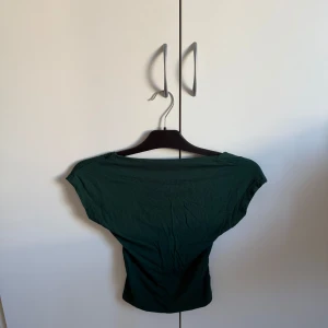 Grön kortärmad topp - Säljer en stilren grön topp med korta ärmar. Toppen har en enkel design och är perfekt för en avslappnad look.  men öppen rygg