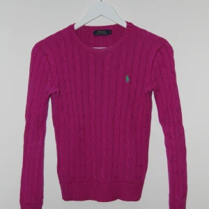 Rosa kabel stickad tröja från Polo Ralph Lauren - Säljer en snygg rosa stickad tröja från Polo Ralph Lauren med det klassiska gröna logotypbroderiet på bröstet. Den är i mycket bra skick och gjord i ett väldigt mjukt och bekvämt material. Den är i storlek xs
