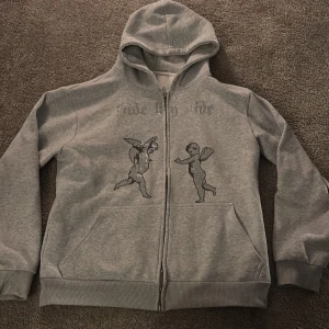 Grå hoodie med änglamotiv - Säljer en grå hoodie med dragkedja och med ett änglamotiv på framsidan. Texten 'Side by Side' storlek S passar M skick 10/10 andvänd få gånger 