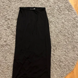 Svart långkjol med knytband - Elegant svart långkjol med knytband i midjan. Perfekt för en stilren look. Kjolen har en enkel och klassisk design som passar till många olika tillfällen.
