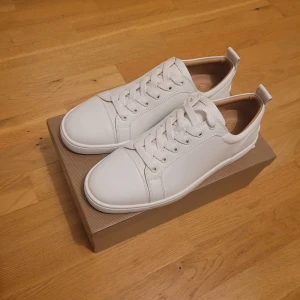 Christian Louboutin - Säljer ett par stilrena vita sneakers från Christian Louboutin i nytt skick. De har den ikoniska röda sulan och är gjorda i skinn med snygg snörning. Perfekta för både vardag och fest! Kommer med originalkartong och dustbag. Lite använda men det är bara smuts tvättar man dom som blir dom som nya